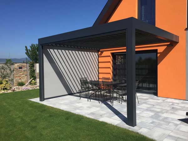 pergola bioclimatique en aluminium noir fermée sur un côté installée sur terrasse et acollée à la maison